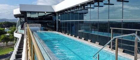 A modern hotel with a large glass pool, outdoor seating, and a view of the surrounding landscape.