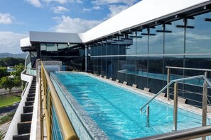 A modern hotel with a large glass pool, outdoor seating, and a view of the surrounding landscape.