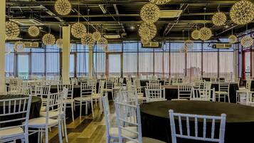 Un salón amplio con mesas redondas y sillas blancas, ventanas grandes y lámparas decorativas colgantes.