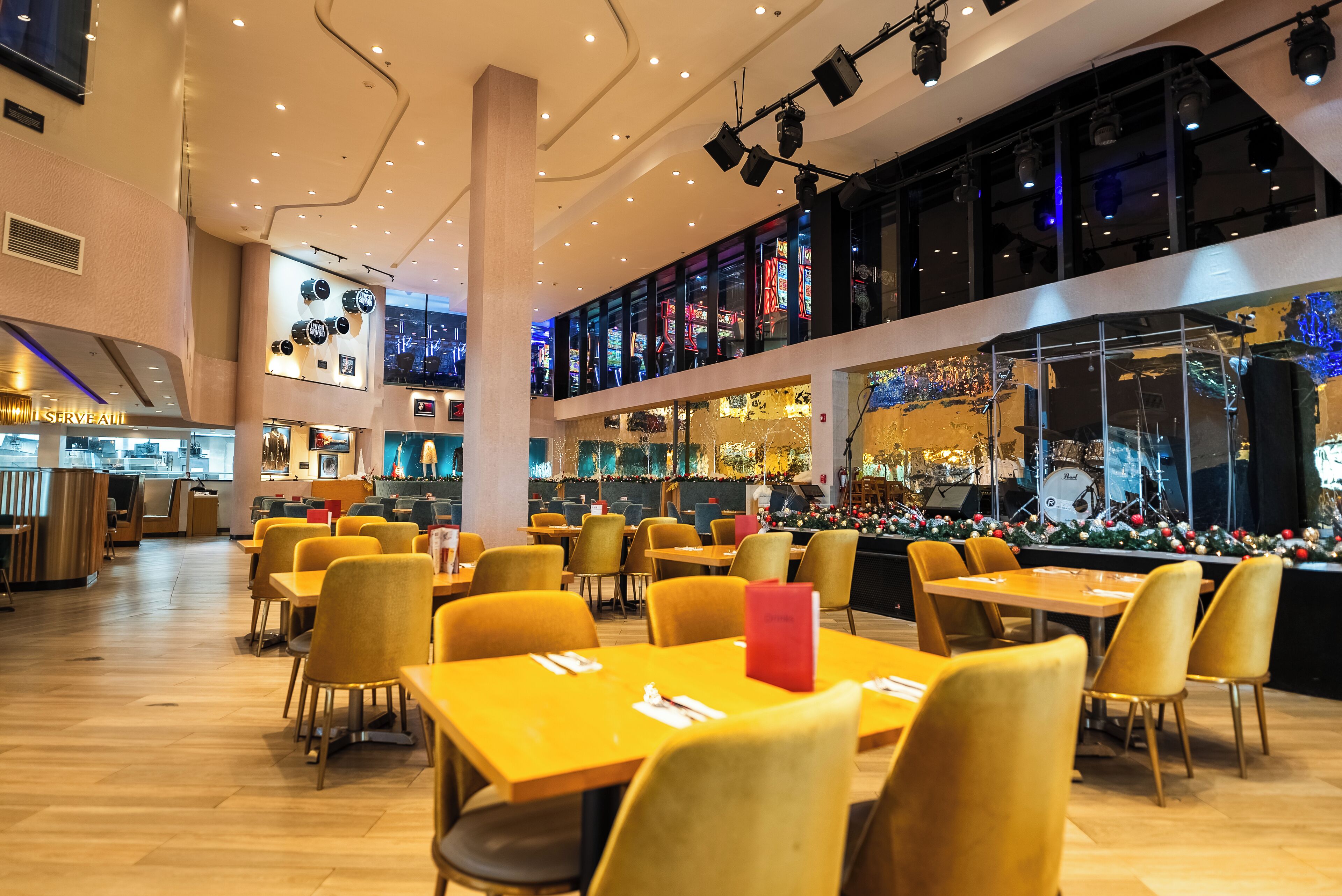 Un restaurante moderno con mesas y sillas amarillas, una zona de bar con decoración navideña y vistas de la ciudad a través de amplias ventanas.