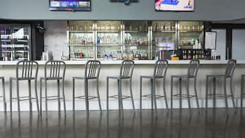 A bar area with a modern design, featuring a bar counter, multiple seating options, and a television mounted above the bar displaying sports content.