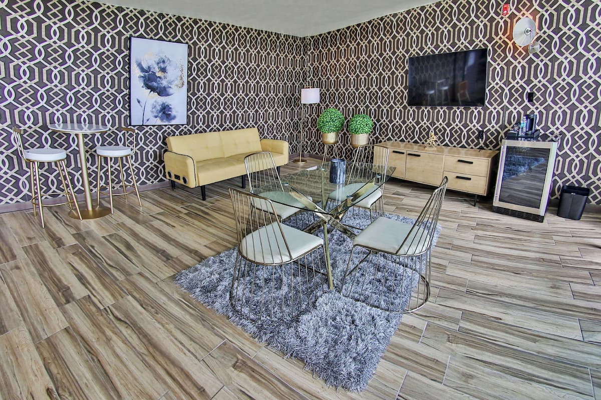 A modern living room with a patterned wallpaper, a glass dining table with chairs, a sofa, a TV, and a cabinet.