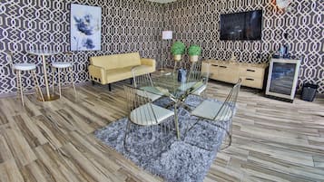 A modern living room with a patterned wallpaper, a glass dining table with chairs, a sofa, a TV, and a cabinet.