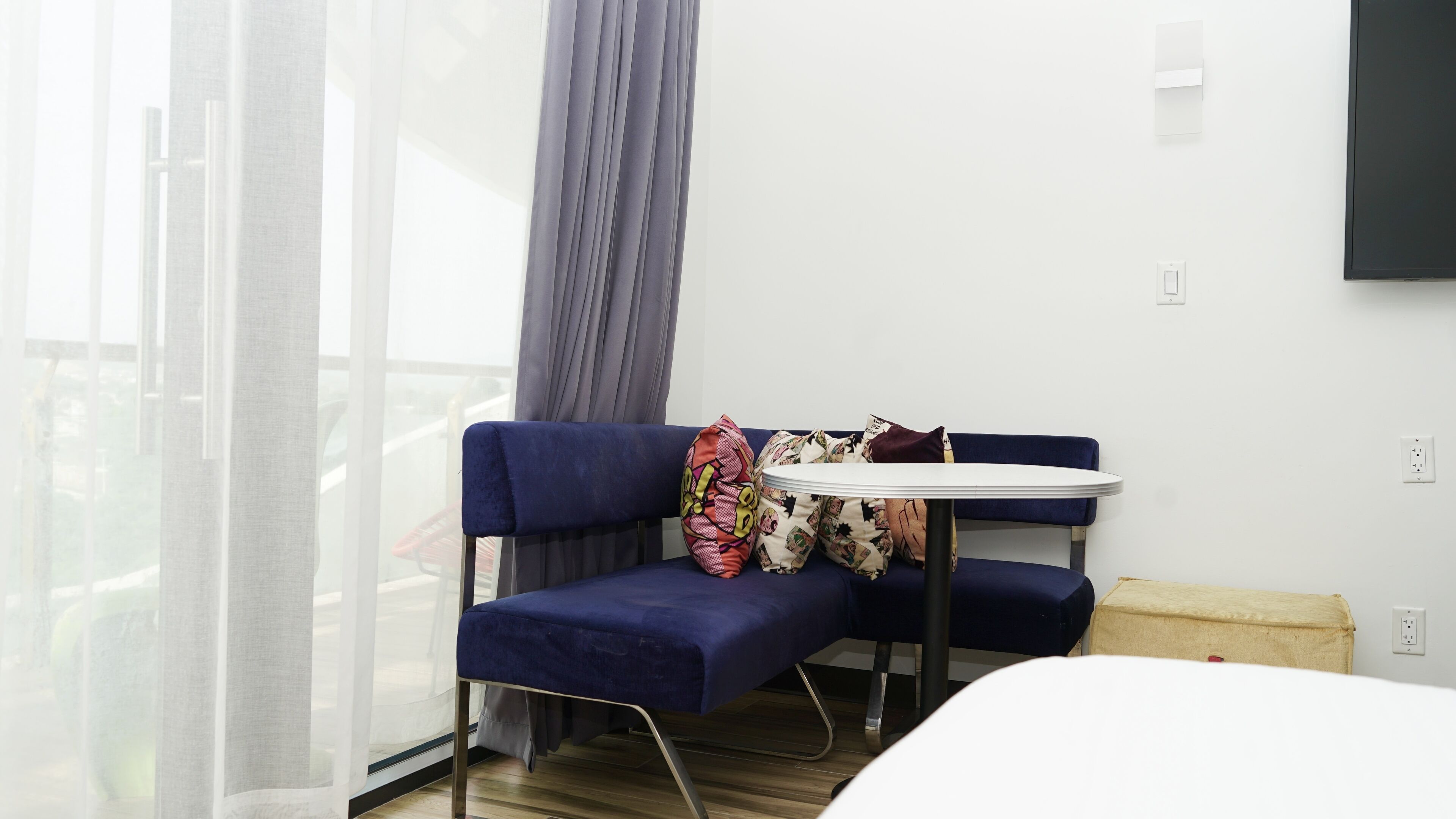 A modern room with a blue sofa, a small round table, and a white chair. There are patterned pillows on the sofa.