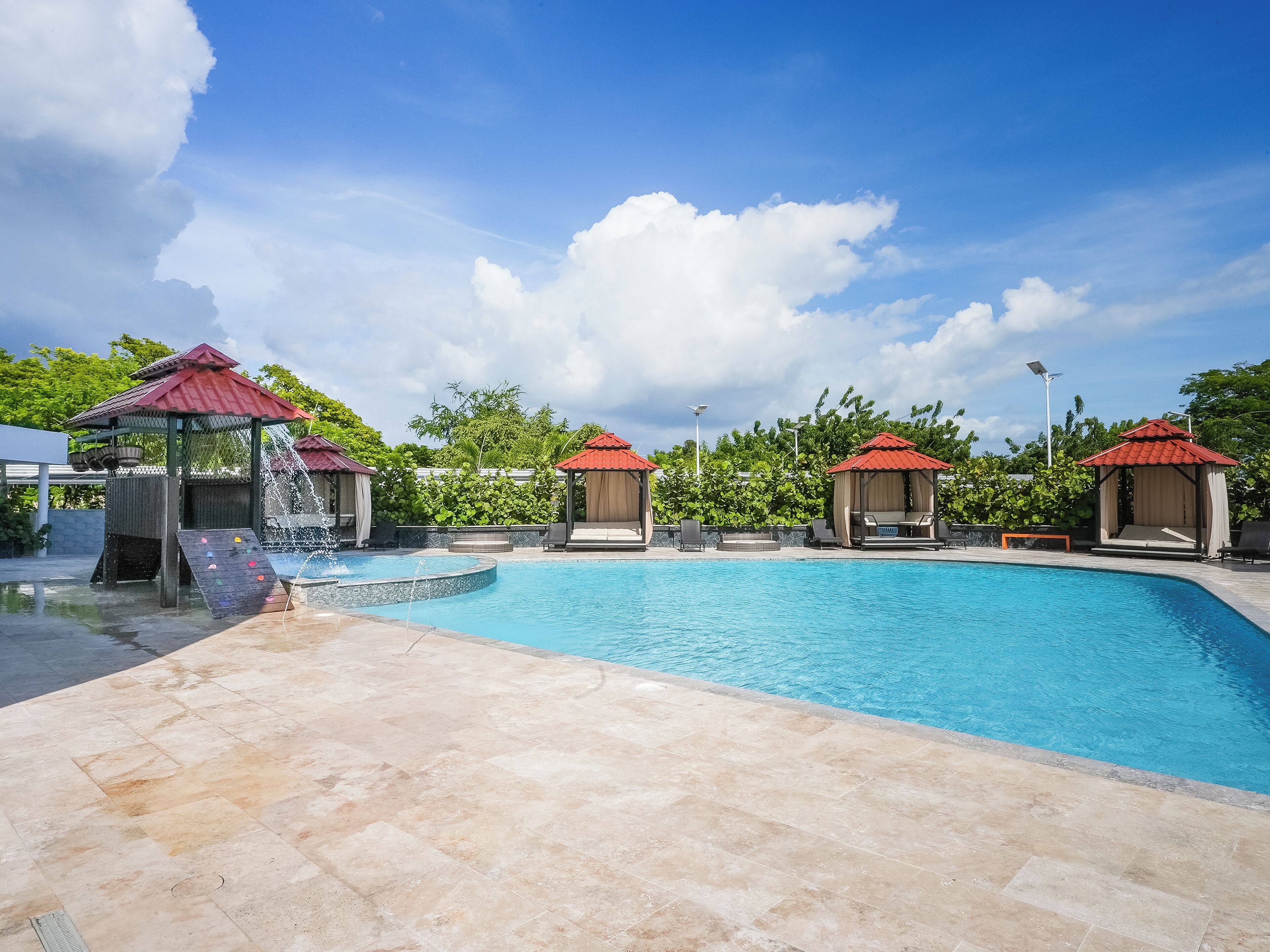 A swimming pool with a red-roofed pavilion, a water slide, and a stone-tiled deck.