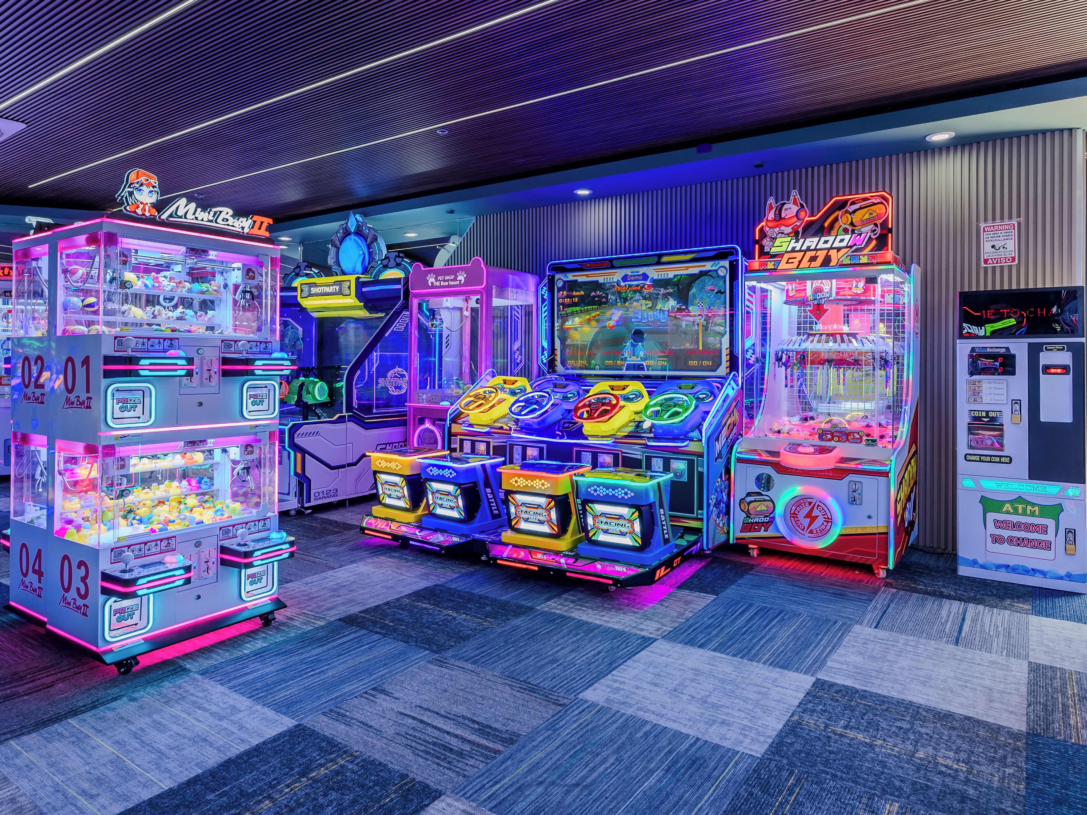Une rangée de bornes d’arcade illuminées de couleurs vives, dans un décor intérieur moderne.