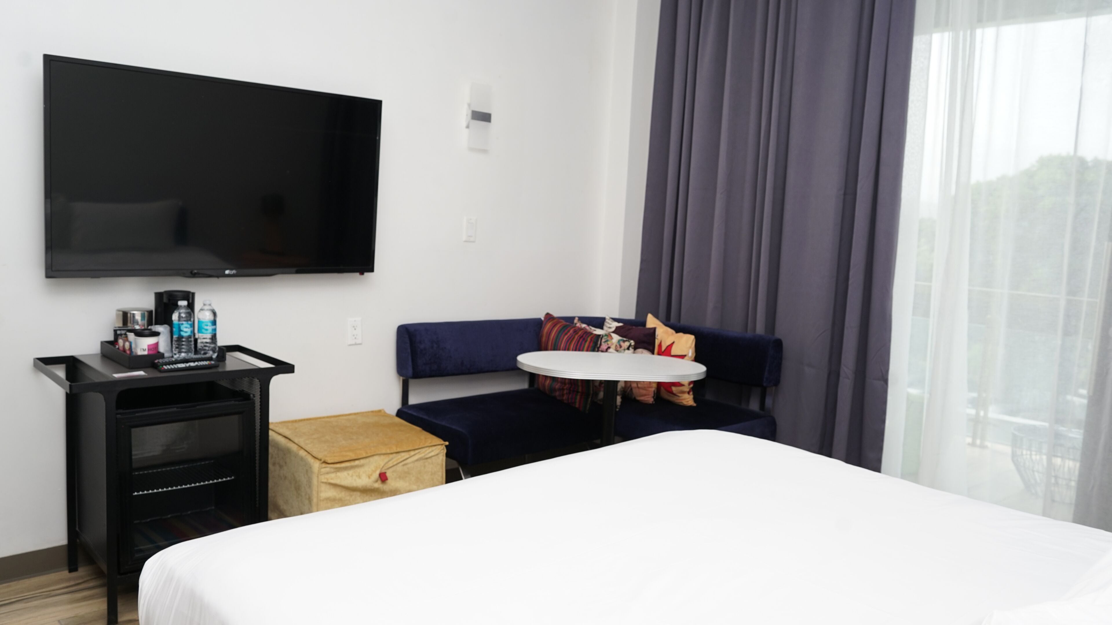 Una habitación de hotel con una cama, televisión, una mesita y un sofá.
