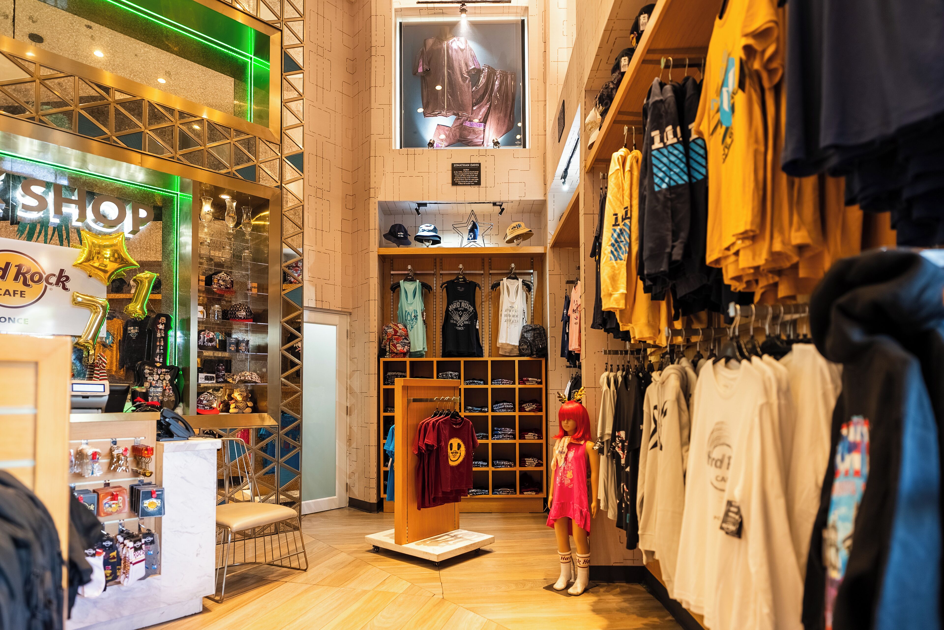 Una tienda de ropa con un maniquí vestido de rosa, estantes con sombreros y un letrero que dice 'Shop'.