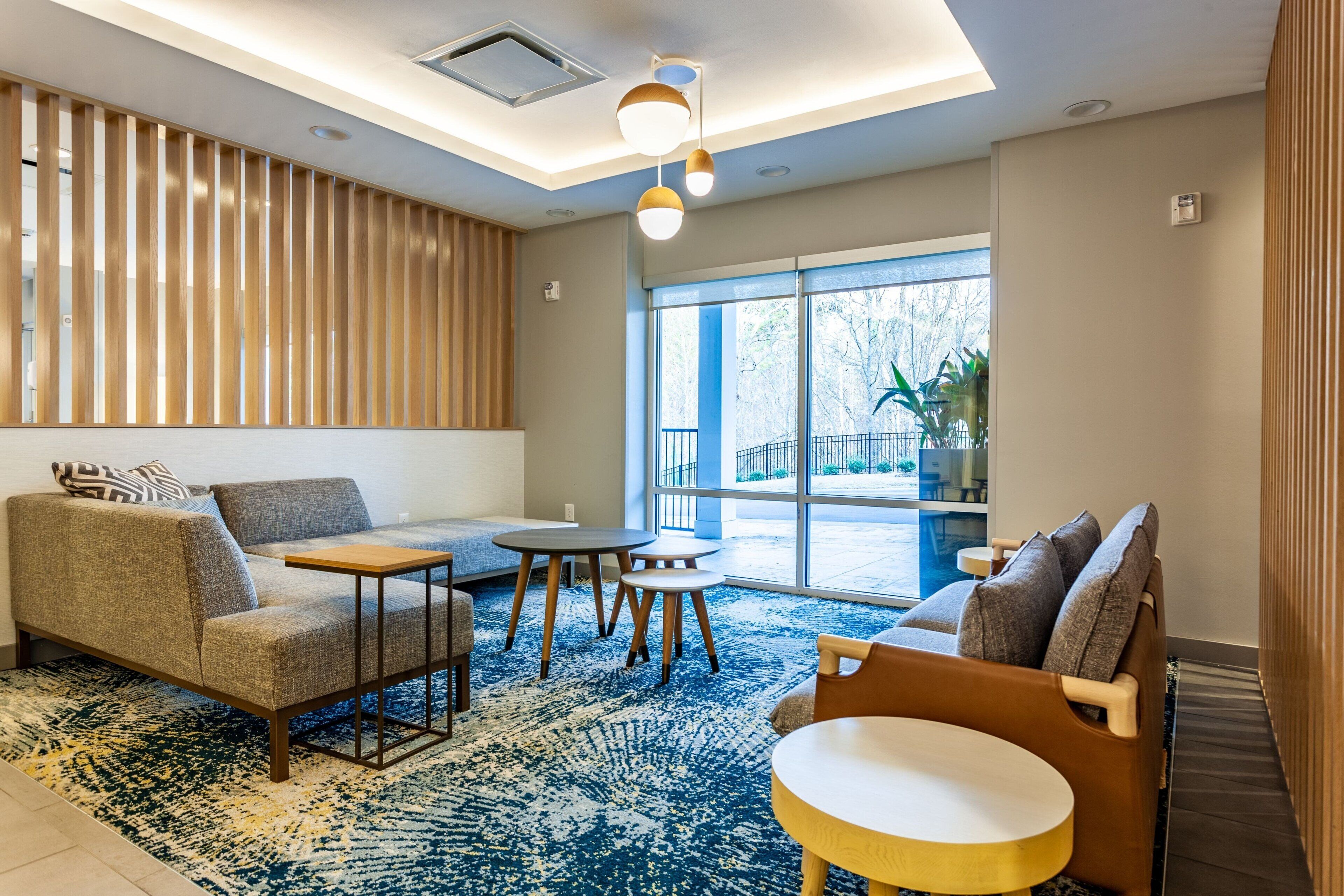A modern hotel lobby with a sofa, armchairs, a small table, and a large window offering a view of the outdoors.