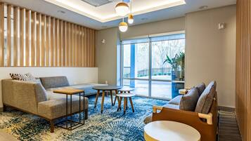 A modern hotel lobby with a sofa, armchairs, a small table, and a large window offering a view of the outdoors.