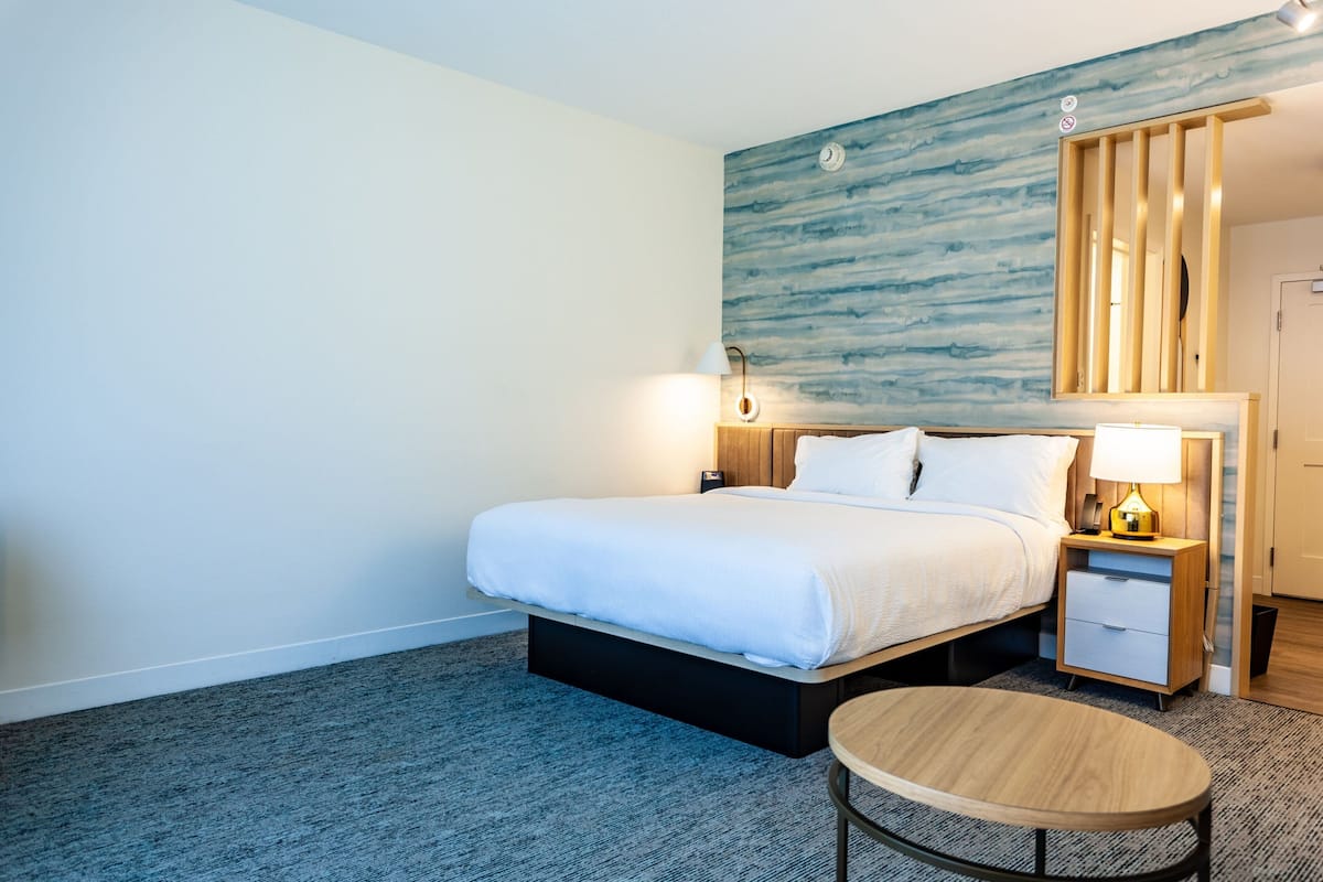 Ein Hotelzimmer mit einem Bett, Nachttischen, einem runden Tisch und einer Wand mit blauem Strukturdesign.