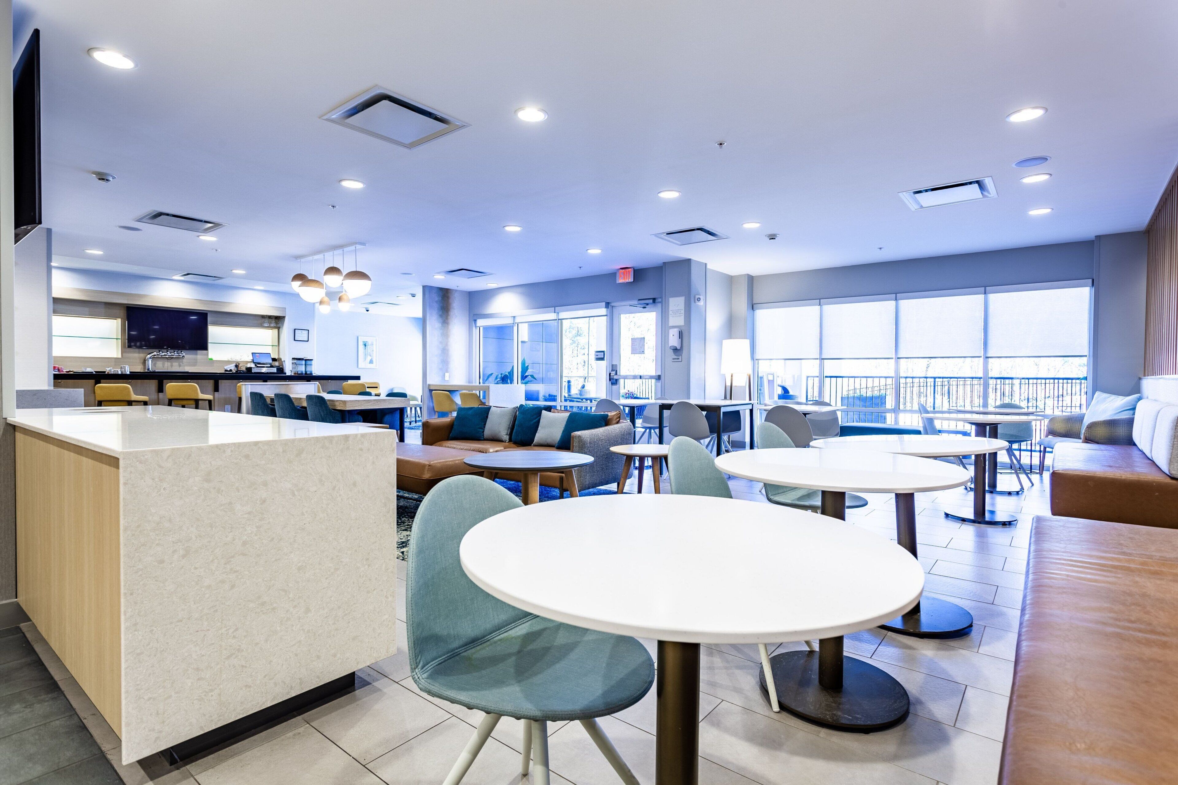 A modern hotel lobby with a reception desk, seating areas, and large windows providing natural light.