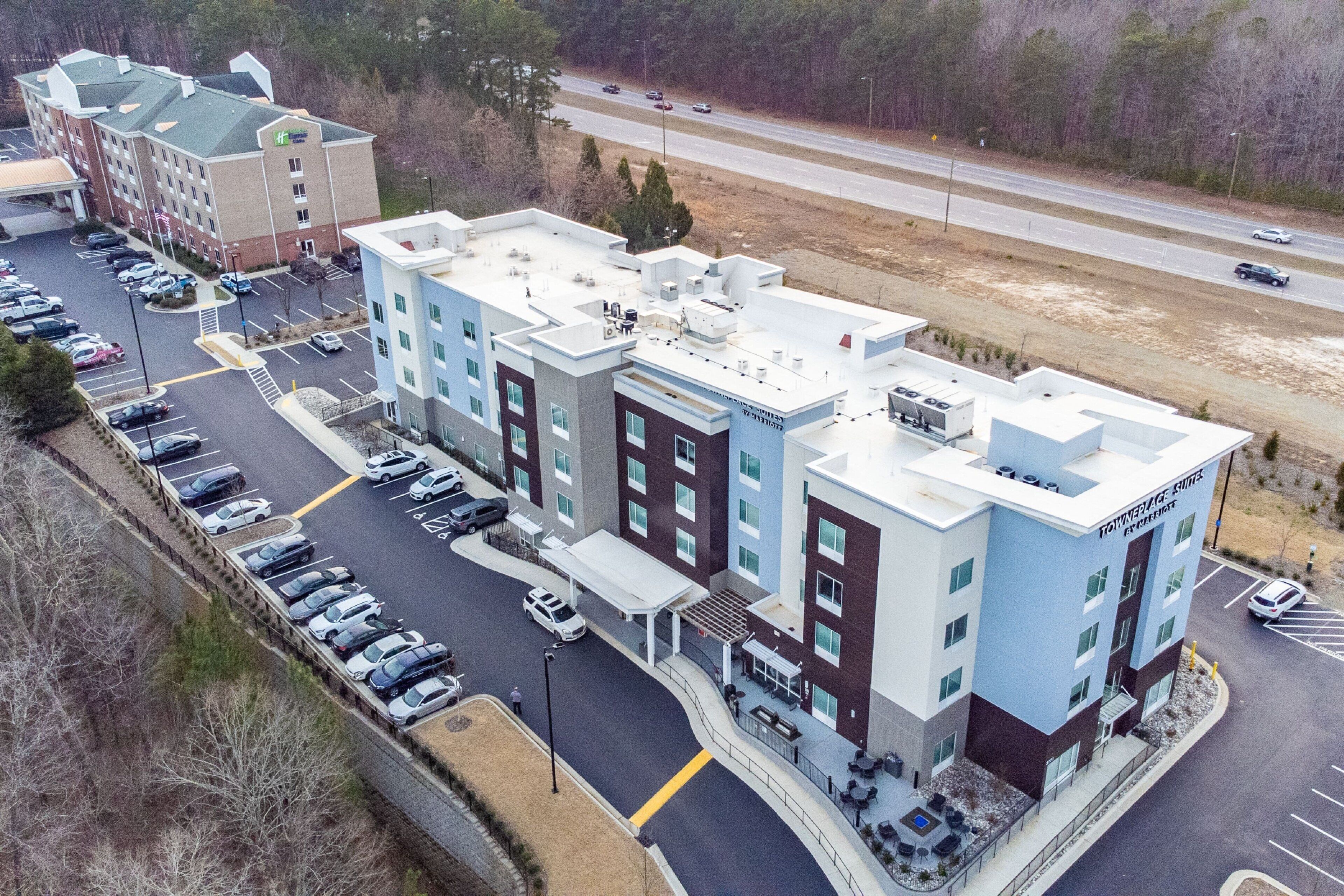 A multi-story hotel with a parking lot, a covered outdoor seating area, and a road in the background.