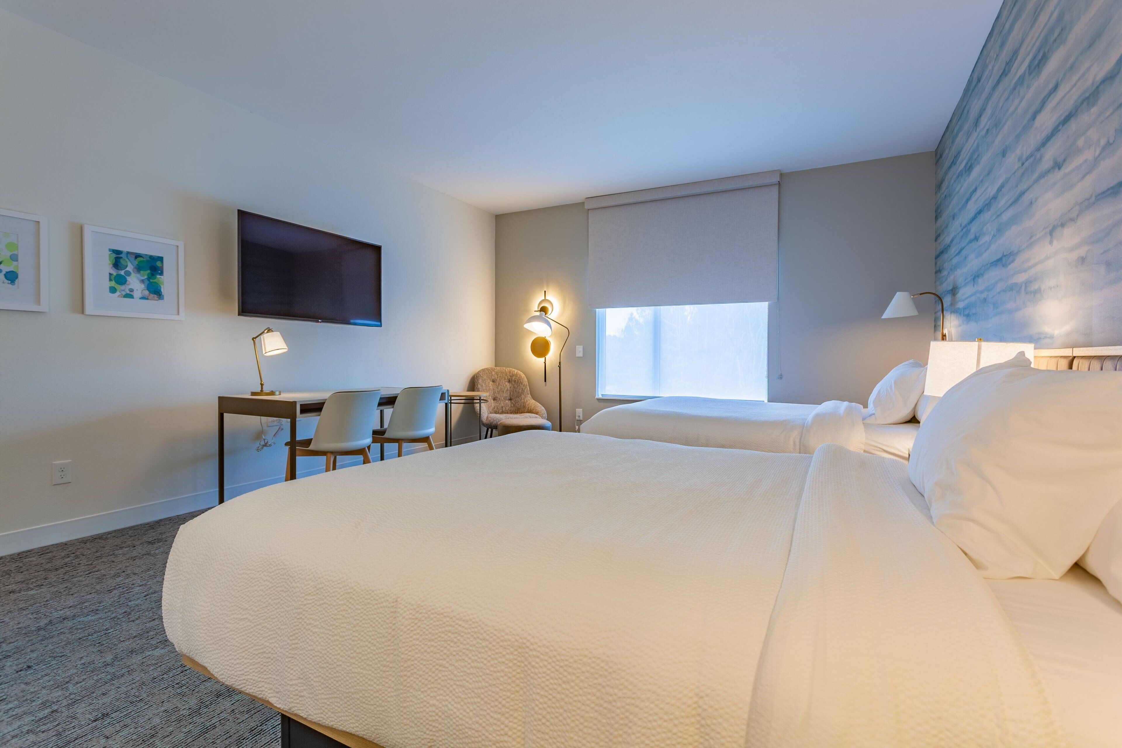 Ein Hotelzimmer mit zwei Betten, einem Schreibtisch, einem Stuhl, einem Fernseher und einem Fenster mit Blick.