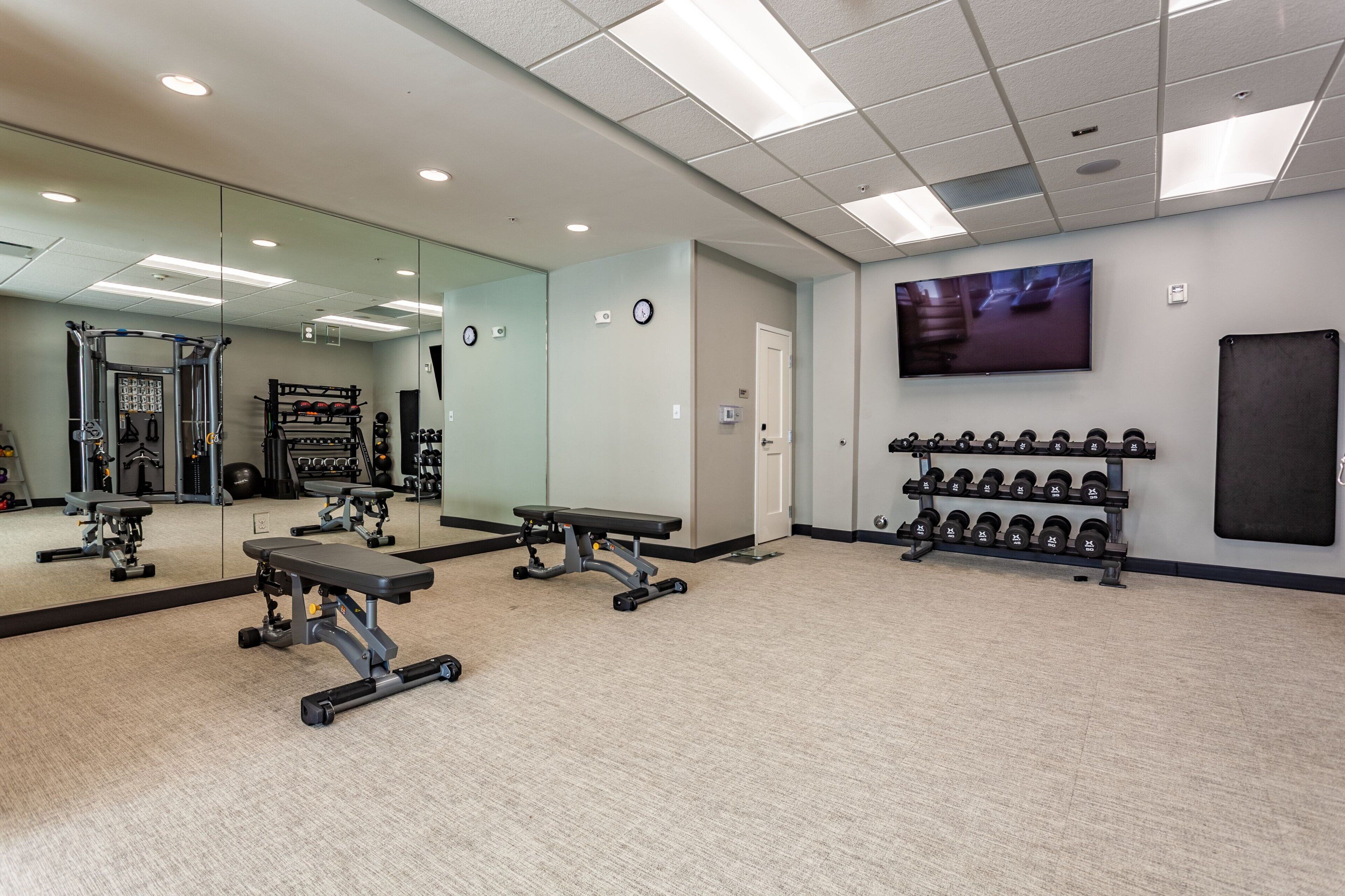A gym with weightlifting equipment, benches, and a TV on the wall.
