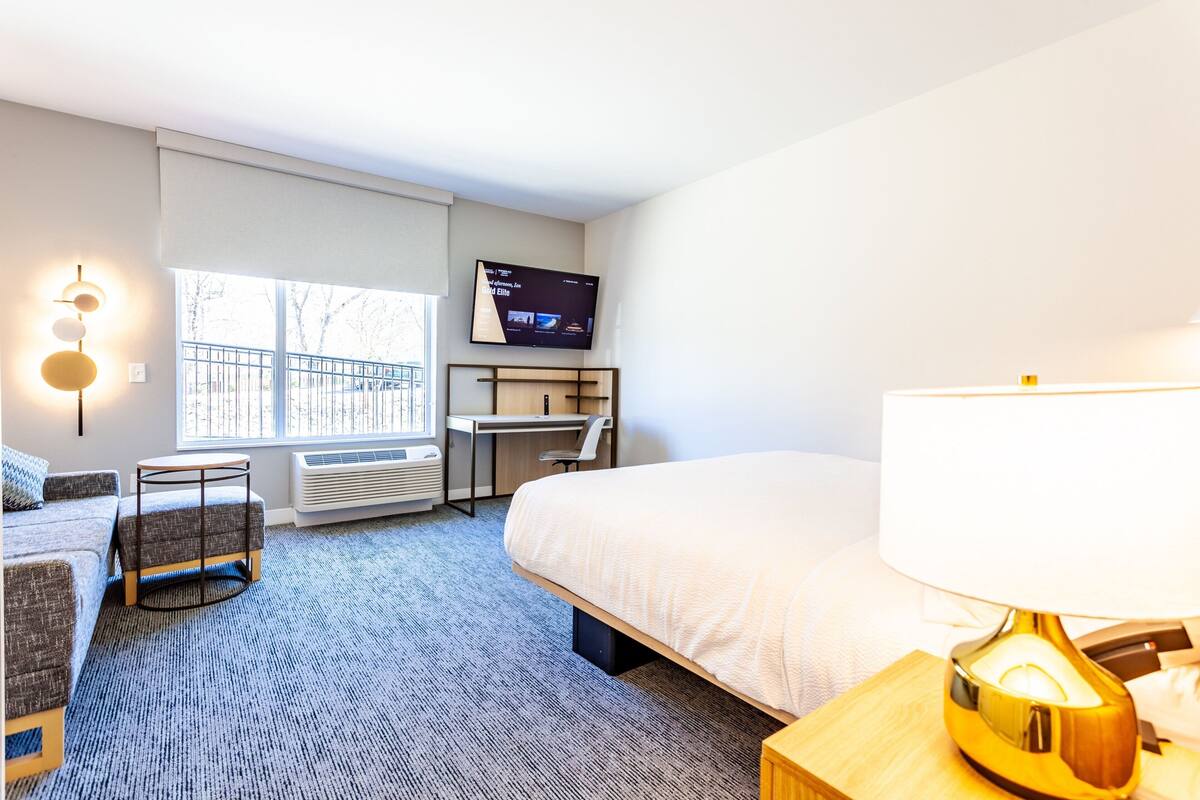Ein Hotelzimmer mit Bett, Schreibtisch, Stuhl, Fernseher und Lampe.