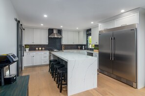 Una cucina moderna con mobili bianchi, un'isola grande con sgabelli da bar, un frigorifero in acciaio inossidabile e uno schienale nero.