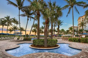 A pool area with lounge chairs and palm trees, surrounded by a brick walkway and a building with balconies. - One of Marriott's most alluring properties on the Atlantic Beach (Palm beach shores)