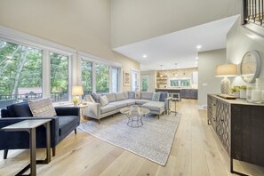 Ein geräumiges Wohnzimmer mit einer großen Eckcouch, einem Couchtisch und einem Essbereich, wobei im Hintergrund eine Küche zu sehen ist.