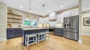 A modern kitchen with white cabinets, a large island with bar stools, a double-door stainless steel refrigerator, and pendant lighting. - High-End Modern Farmhouse Relaxation in Saugatuck - Close to Downtown (Saugatuck)