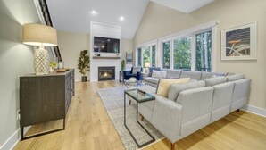 A modern living room with a grey sectional sofa, a glass coffee table, and a fireplace. - High-End Modern Farmhouse Relaxation in Saugatuck - Close to Downtown (Saugatuck)