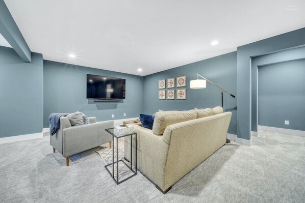Ein Wohnzimmer mit grauem Sofa, einem weißen Sessel, einem kleinen Couchtisch und einem flachbildfernseher, der an der Wand montiert ist.
