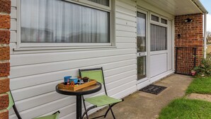 A house with white siding, a brick section, and a small patio with a table and chairs. - 2 bedroom accommodation in Kessingland (Kessingland)