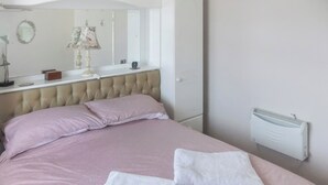 A neatly made bed with pink bedding and white towels, a tufted headboard, a bedside table with a lamp, and a mirror above it. - 2 bedroom accommodation in Kessingland (Kessingland)