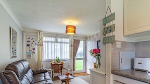 A modern living room with a leather sofa, a dining table with chairs, a kitchen area with white cabinets, and decorative signs on the wall. - 2 bedroom accommodation in Kessingland (Kessingland)