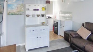 A compact living space with a kitchenette, a white cabinet with decorative items, a brown sofa, and a purple pendant light. - 2 bedroom accommodation in Kessingland (Kessingland)