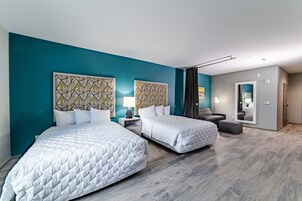 Una habitación de hotel moderna con dos camas queen, paredes color verde azulado, decoración mural geométrica y un espejo grande.
