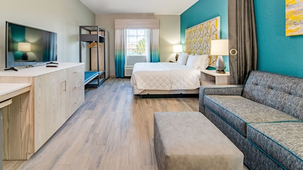 A modern hotel room with a bed, a sofa, a TV, a desk, and a wardrobe. - Everglades Adventures Hotel Suites by Ivey House (Everglades City)