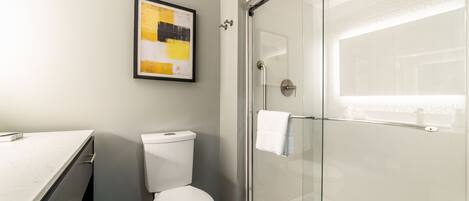 A modern bathroom with a glass shower enclosure, a toilet, and a marble floor.