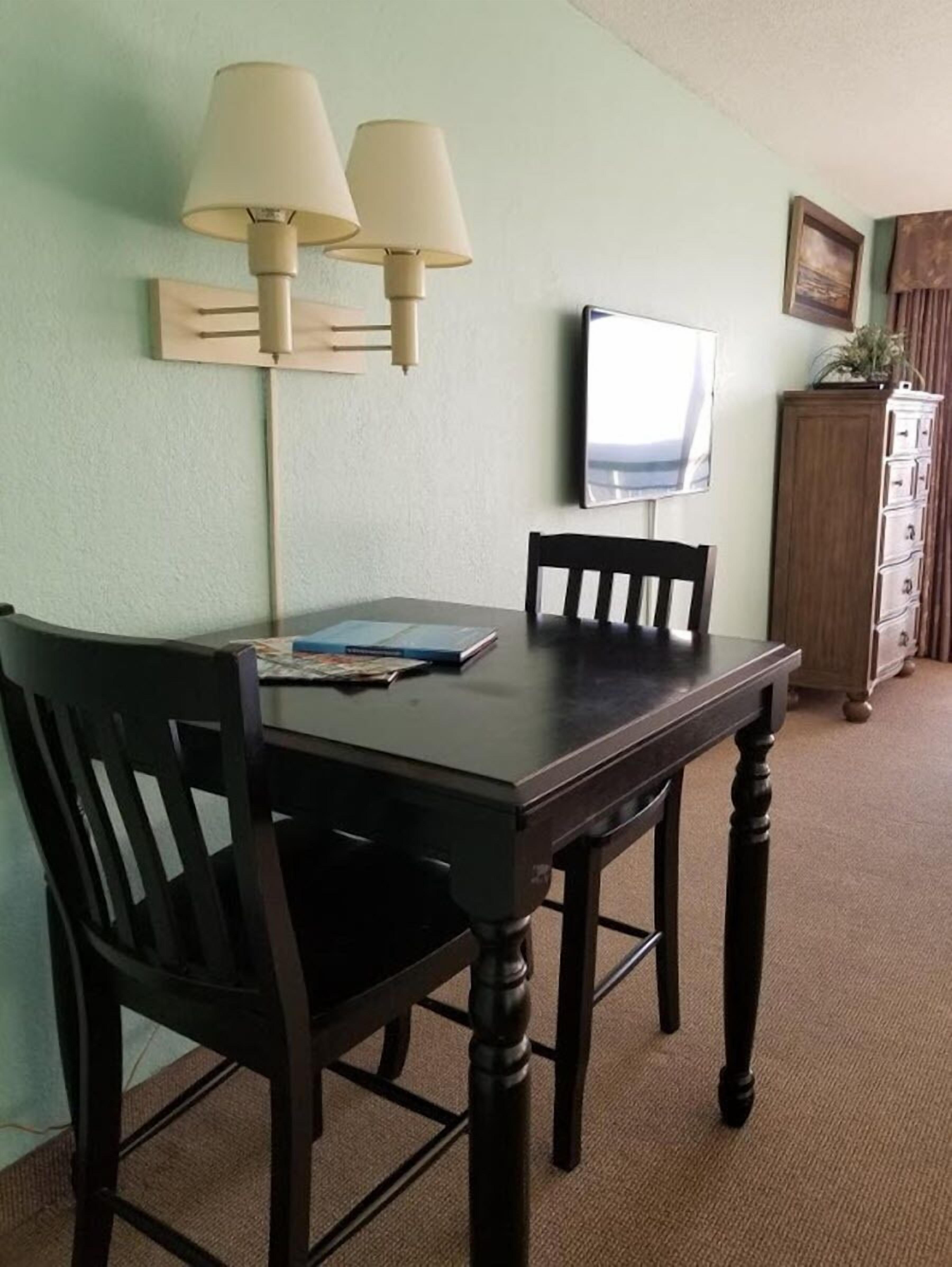 Uma sala de jantar com uma mesa de madeira escura, duas cadeiras e um candeeiro fixado na parede.