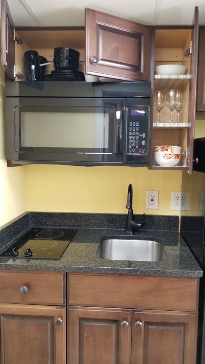 A compact kitchen with a built-in microwave, a sink, and wooden cabinets.