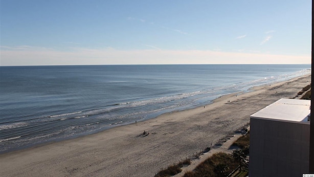 Een strand met een helder uitzicht op de oceaan en een gebouw op de voorgrond.