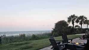 Een terras buiten met een vuurkuil, zitplaatsen en uitzicht op het strand.
