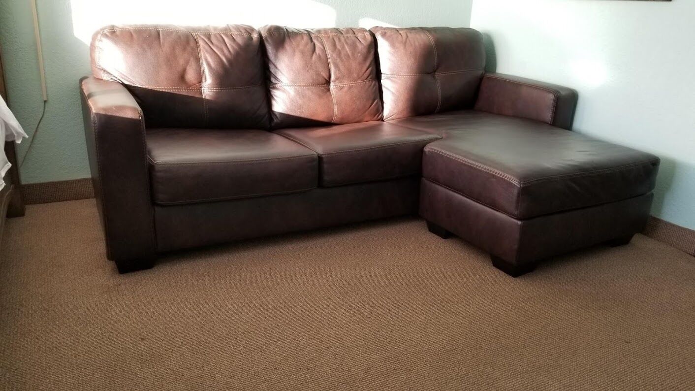 A brown leather sectional sofa with a chaise and a footrest in a room with a carpeted floor.