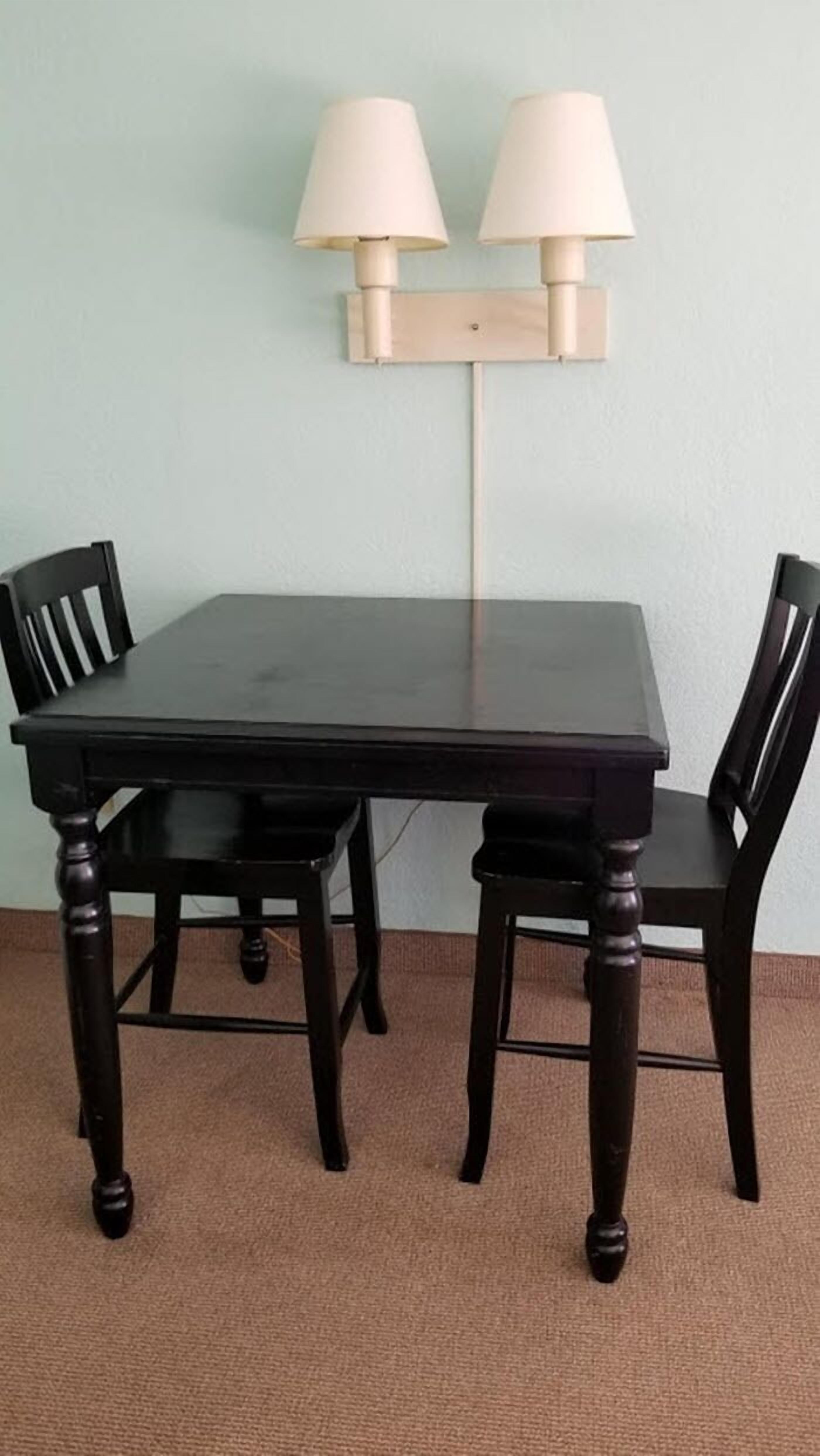 Un tavolo rettangolare da pranzo con quattro sedie, due lampade a parete e un pavimento coperto da tappeto.