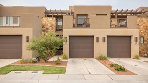 A modern two-story residential building with a stone facade, a covered balcony, and a well-maintained front yard.
