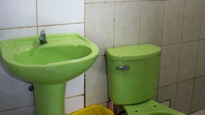 Un baño con lavamanos e inodoro verdes, paredes de azulejos blancos y un espejo.