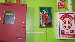 Una pared con varios objetos, incluyendo una caja roja etiquetada 'Mircom', una pared verde con un letrero que dice 'Botiquín' y una imagen enmarcada de una figura religiosa.