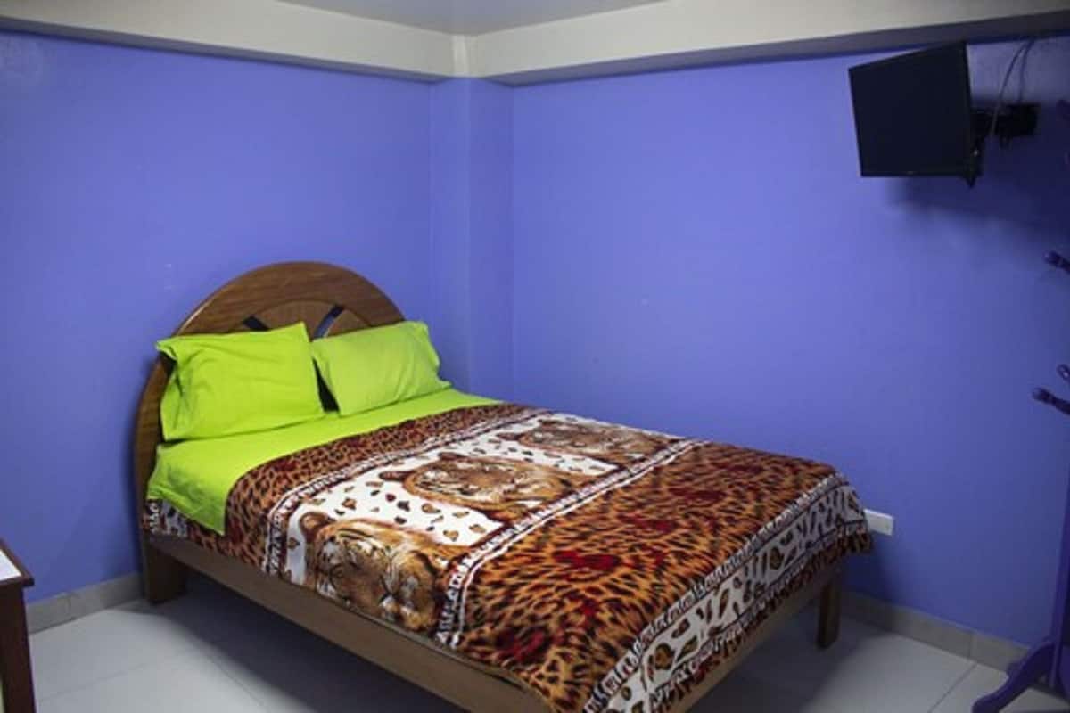 Un dormitorio con cama, cabecera de madera, pared azul y televisor montado en la pared.