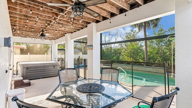 A glass-top table with chairs, a ceiling fan, and a view of a swimming pool.