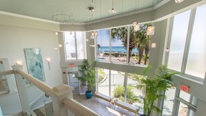 A spacious indoor area with large windows overlooking a pool and beach, featuring potted plants and modern lighting.