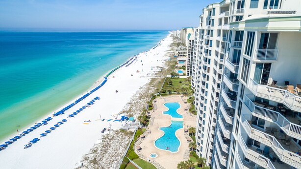 A beachfront hotel with a pool, beach umbrellas, and a clear view of the ocean.