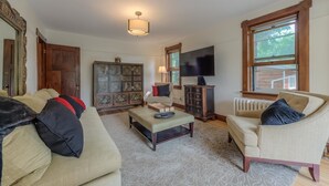 A living room with a sofa, armchair, and a cabinet with decorative panels. There is a television and a window with a view of greenery. - Downtown Delight off Pearl street (Boulder)
