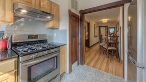 A kitchen with a stove, oven, and wooden cabinets. There is a dining area with a table and chairs visible through an open door. - Downtown Delight off Pearl street (Boulder)