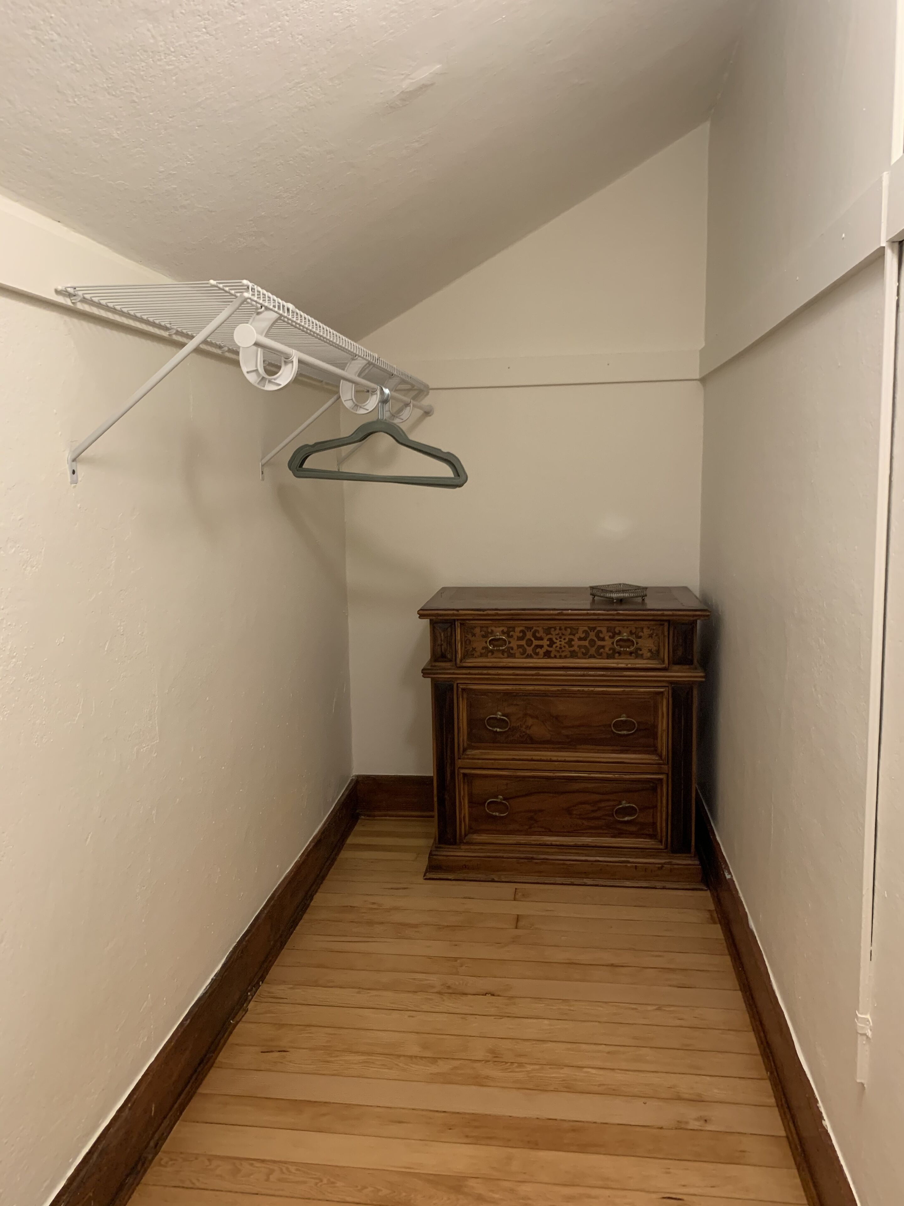Ein schmaler Flur mit Holzboden, weißer Wand und einer Holzkommode mit Schubladen.