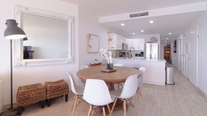 Un espace repas moderne avec une table ronde en bois, des chaises blanches et des bancs en osier.